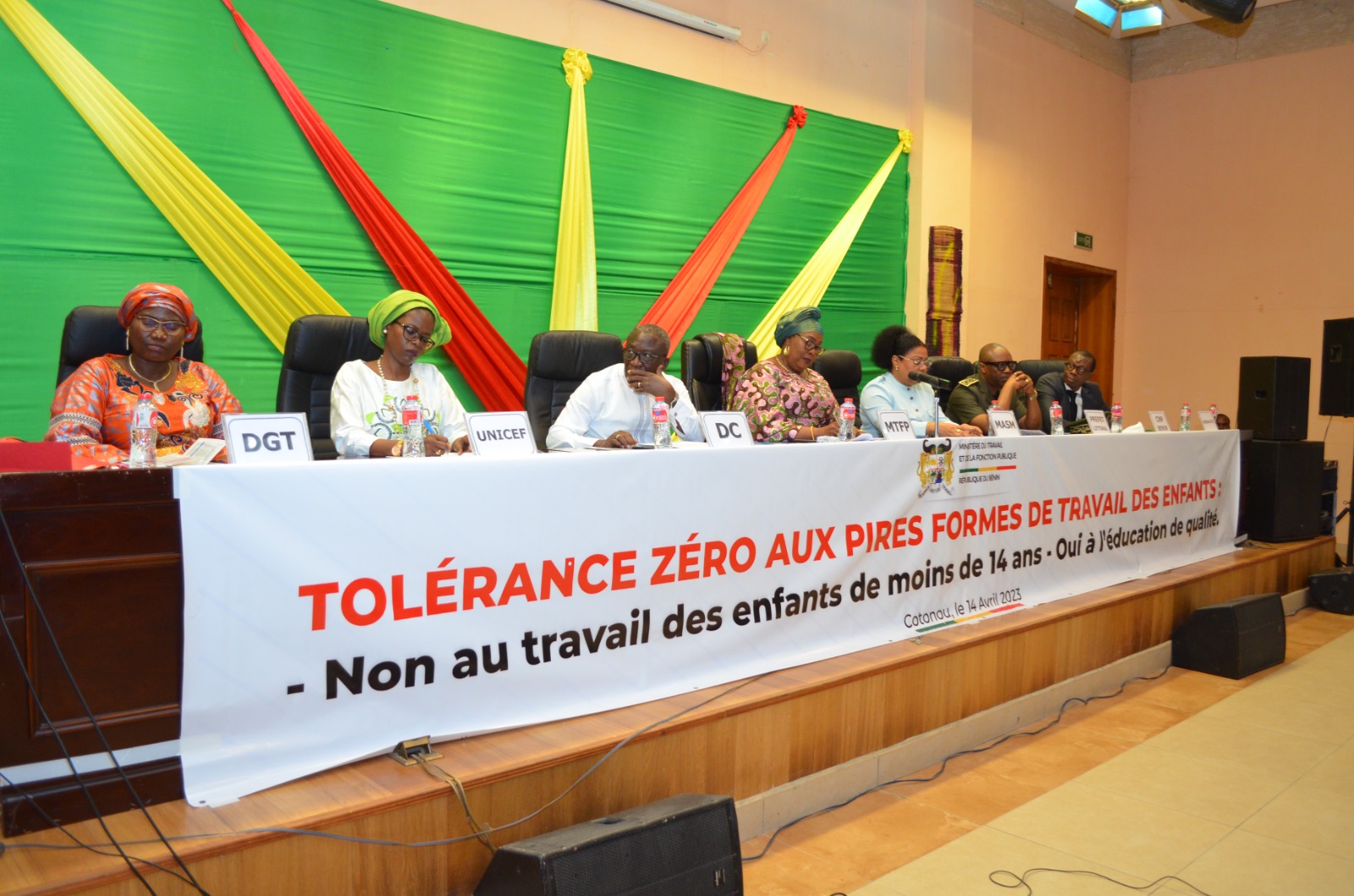 Huit personnes assises derrière une table avec une grande banderole portant un message contre le travail des enfants