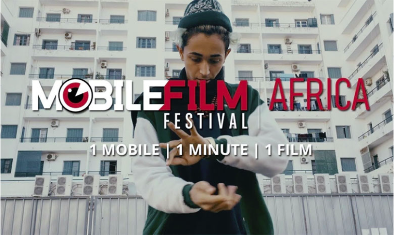 Jeune homme debout en extérieur devant des immeubles, effectuant un geste avec ses mains, texte Mobile Film Festival Africa en surimpression