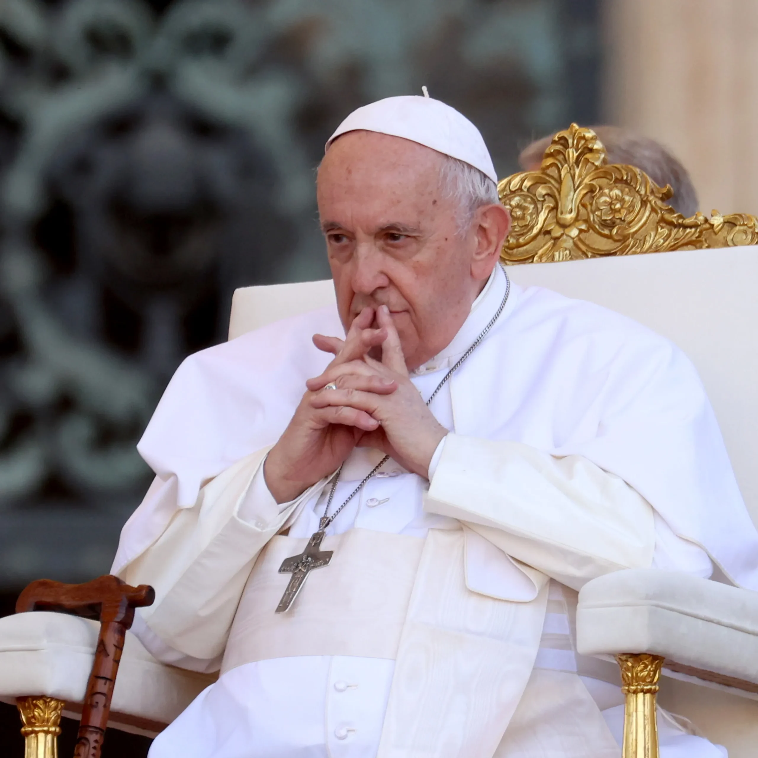Un homme âgé en habit blanc et calotte réfléchit en joignant ses doigts devant son visage assis sur un fauteuil orné d or