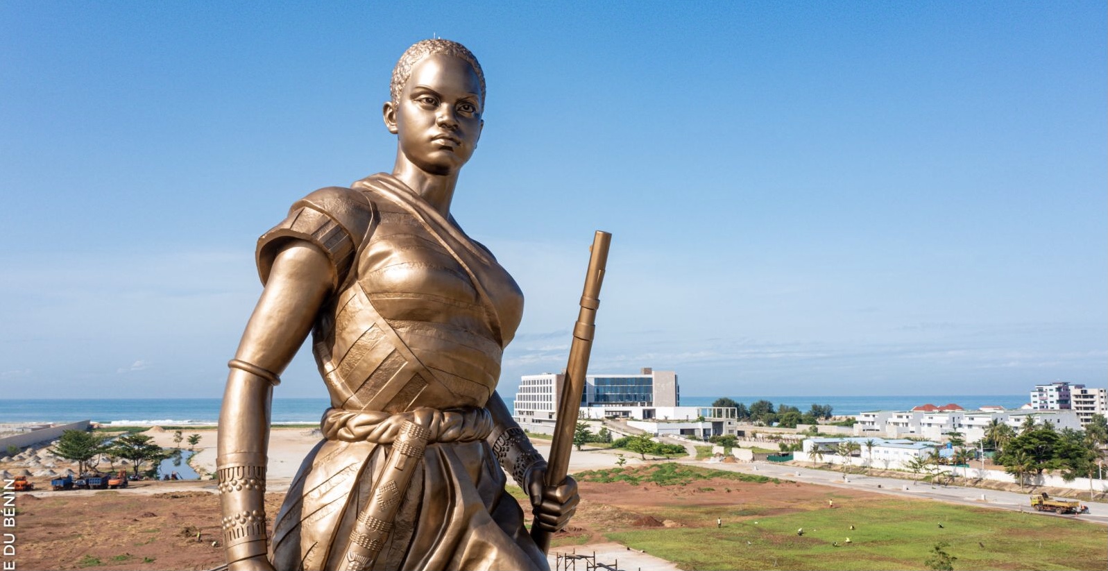 Statue en bronze d'une femme tenant un fusil, avec un paysage urbain et la mer en arrière-plan