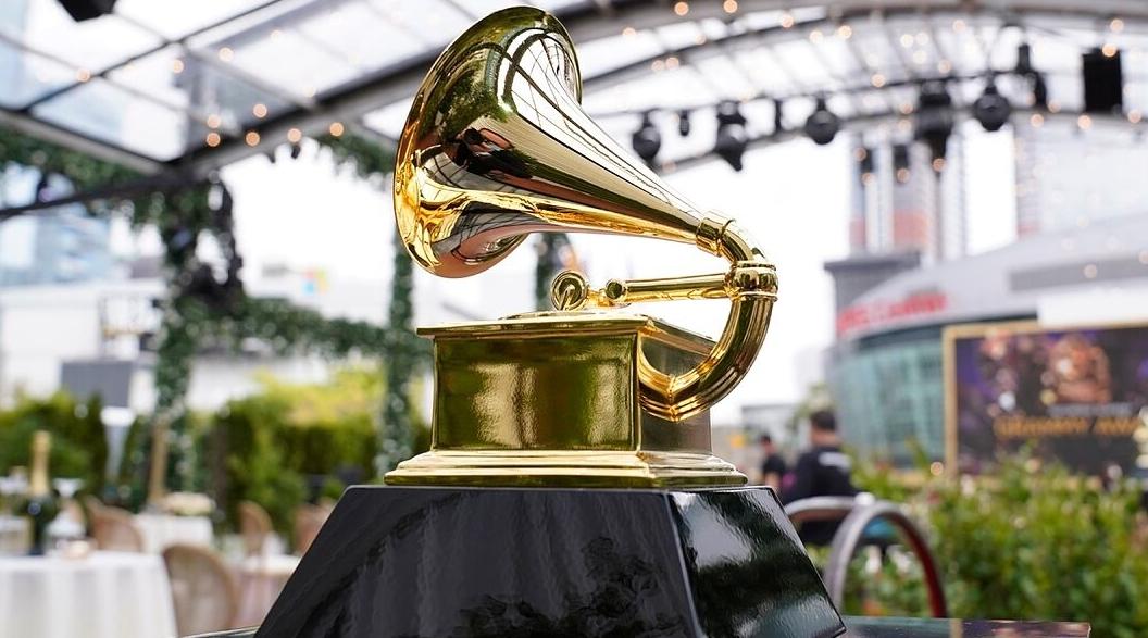 Trophée doré en forme de gramophone posé sur un socle noir dans un espace lumineux avec tables et chaises floues en arrière-plan