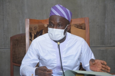Homme en tenue blanche et masque facial assis à une table et parlant lors d’une réunion