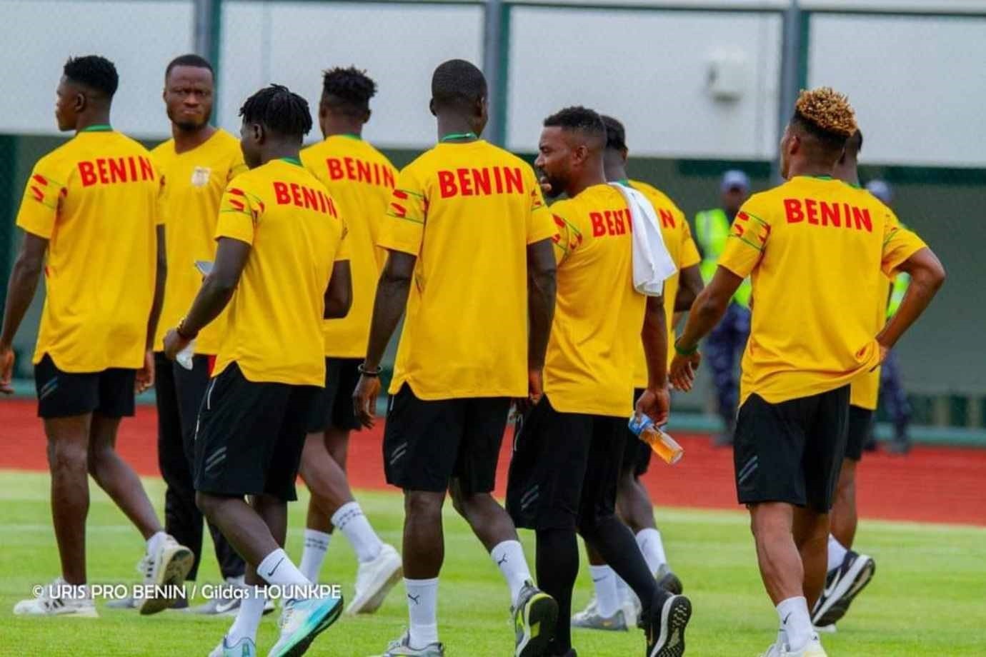 Des joueurs en tenue jaune avec inscription rouge Benin marchent sur un terrain de sport extérieur