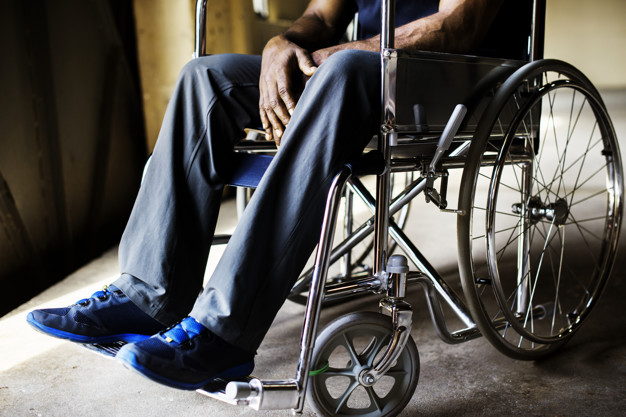Personne assise dans un fauteuil roulant avec des chaussures bleues et un pantalon gris dans un intérieur sombre