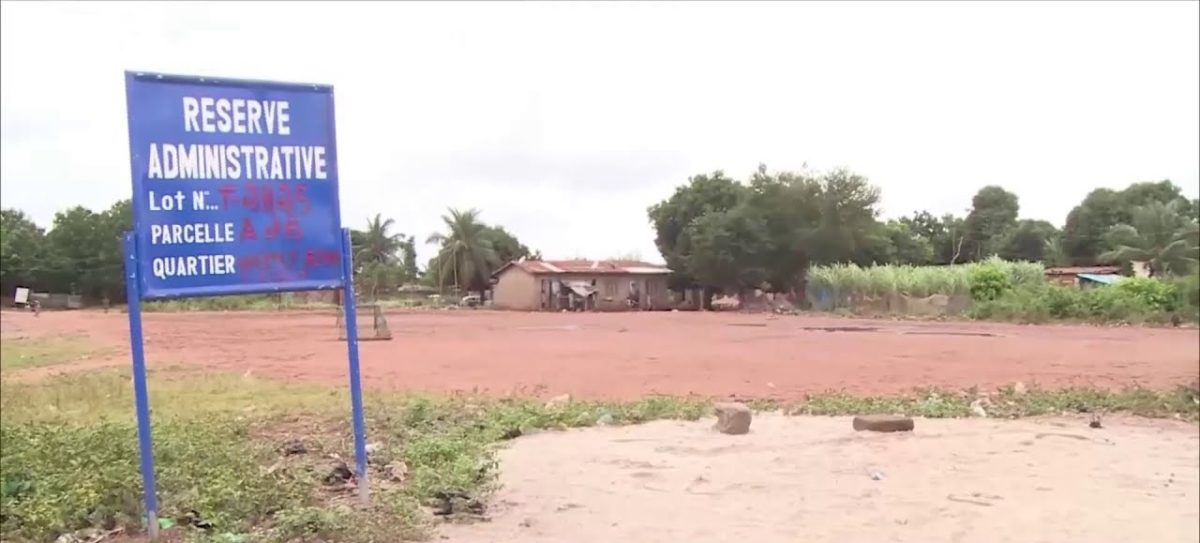 Terrain vague délimité par un panneau bleu indiquant une réserve administrative avec une maison et des arbres en arrière-plan