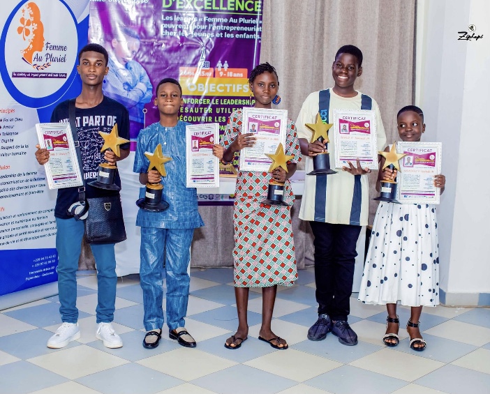 Cinq enfants debout tenant chacun un trophée étoile et un certificat devant un mur avec des affiches colorées