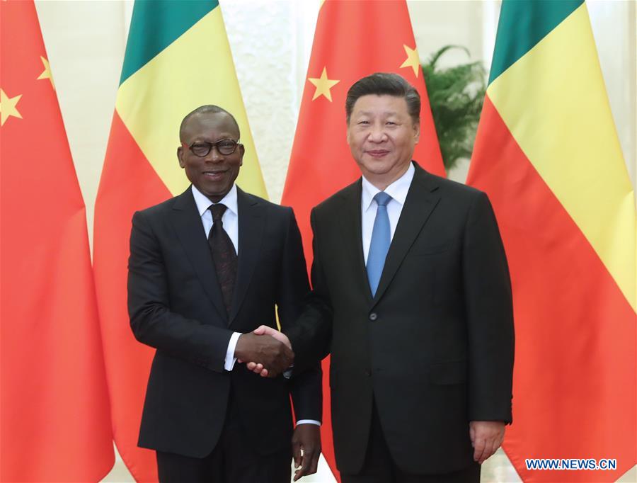 Deux hommes en costume sombre se serrent la main devant trois drapeaux chinois et deux drapeaux jaunes et verts