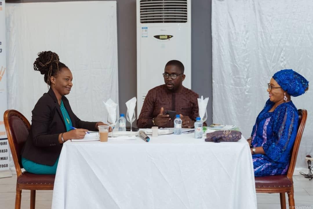 Trois personnes échangent autour d’une table blanche dans une salle avec un climatiseur mural
