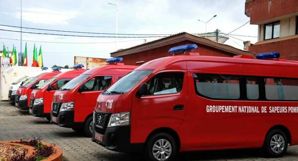 Plusieurs véhicules rouges de secours alignés devant un bâtiment sous un ciel nuageux