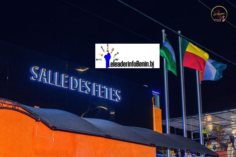 Enseigne lumineuse « SALLE DES FETES » avec trois drapeaux sur des mats devant un bâtiment orange la nuit