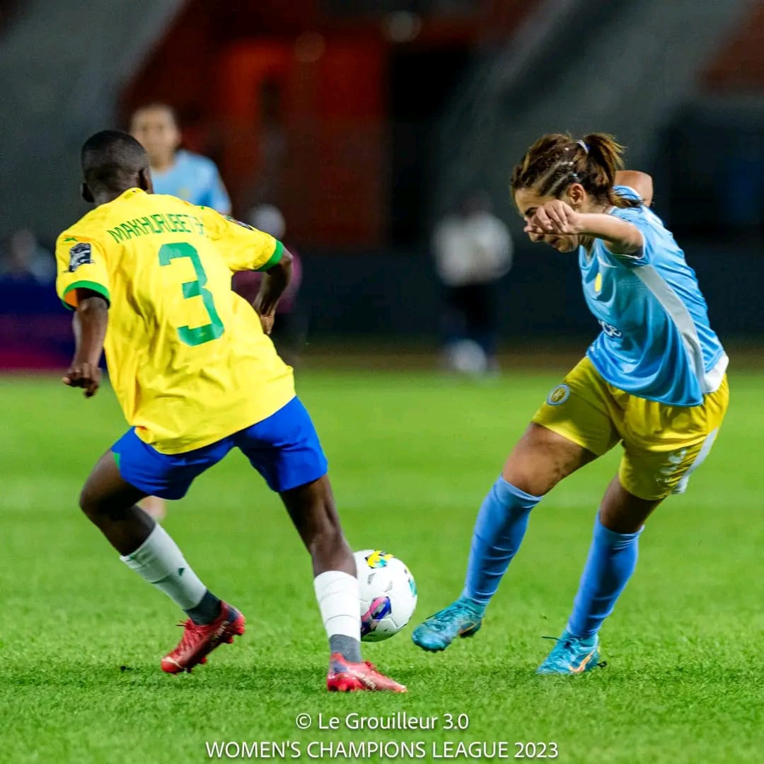 Deux joueuses de football en duel pour le contrôle du ballon sur un terrain vert lors d’un match nocturne