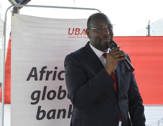 Un homme en costume sombre parle dans un micro devant une bannière avec le texte partiel UBA Africa global bank