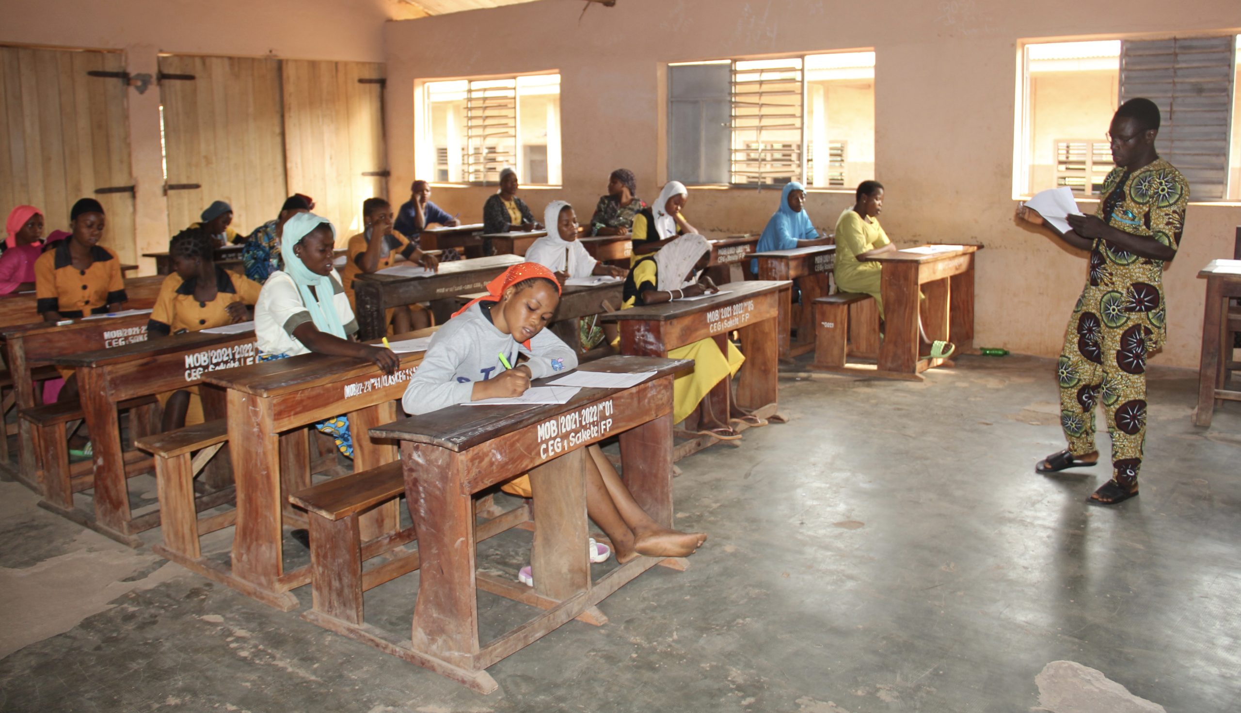 Salle de classe avec des adultes assis à des pupitres et un homme debout leur lisant un document