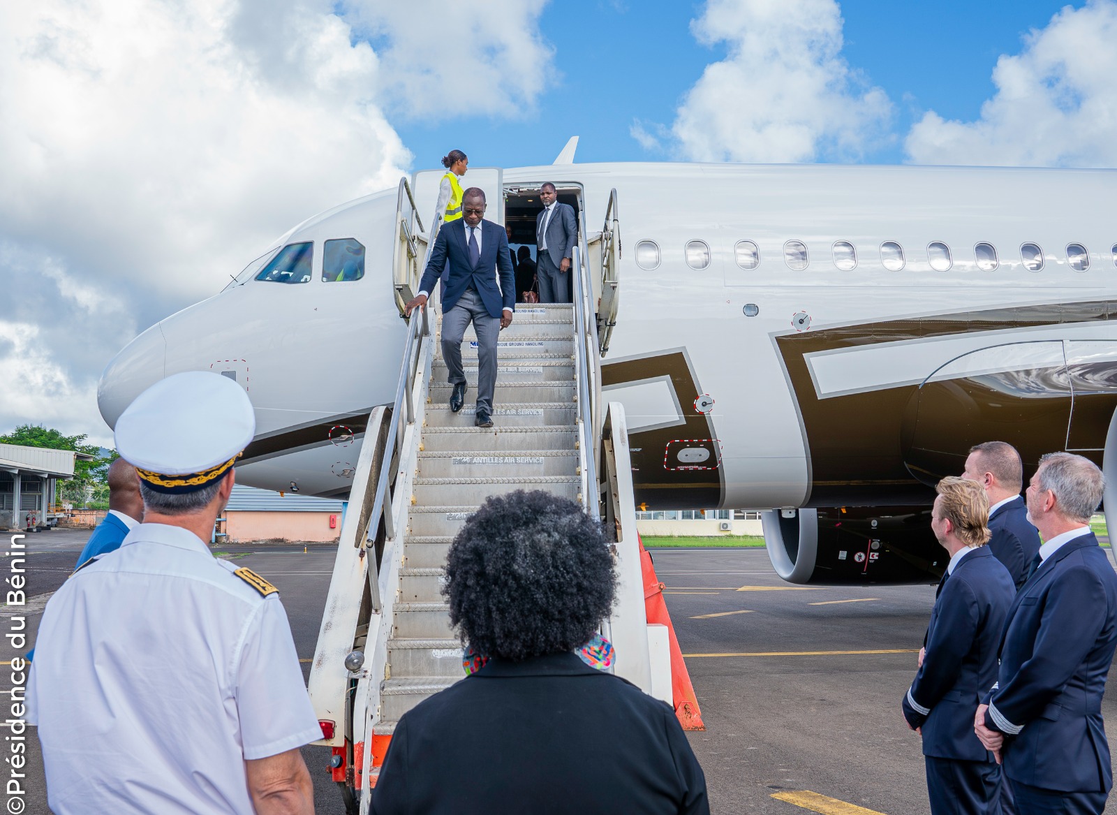 Un homme descend d’un avion sur le tarmac accueilli par plusieurs personnes dont un officier en uniforme blanc