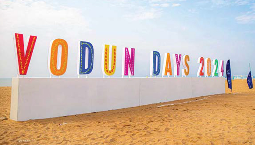 Grandes lettres colorées formant le texte VODUN DAYS 2024 posées sur un socle blanc sur une plage sableuse