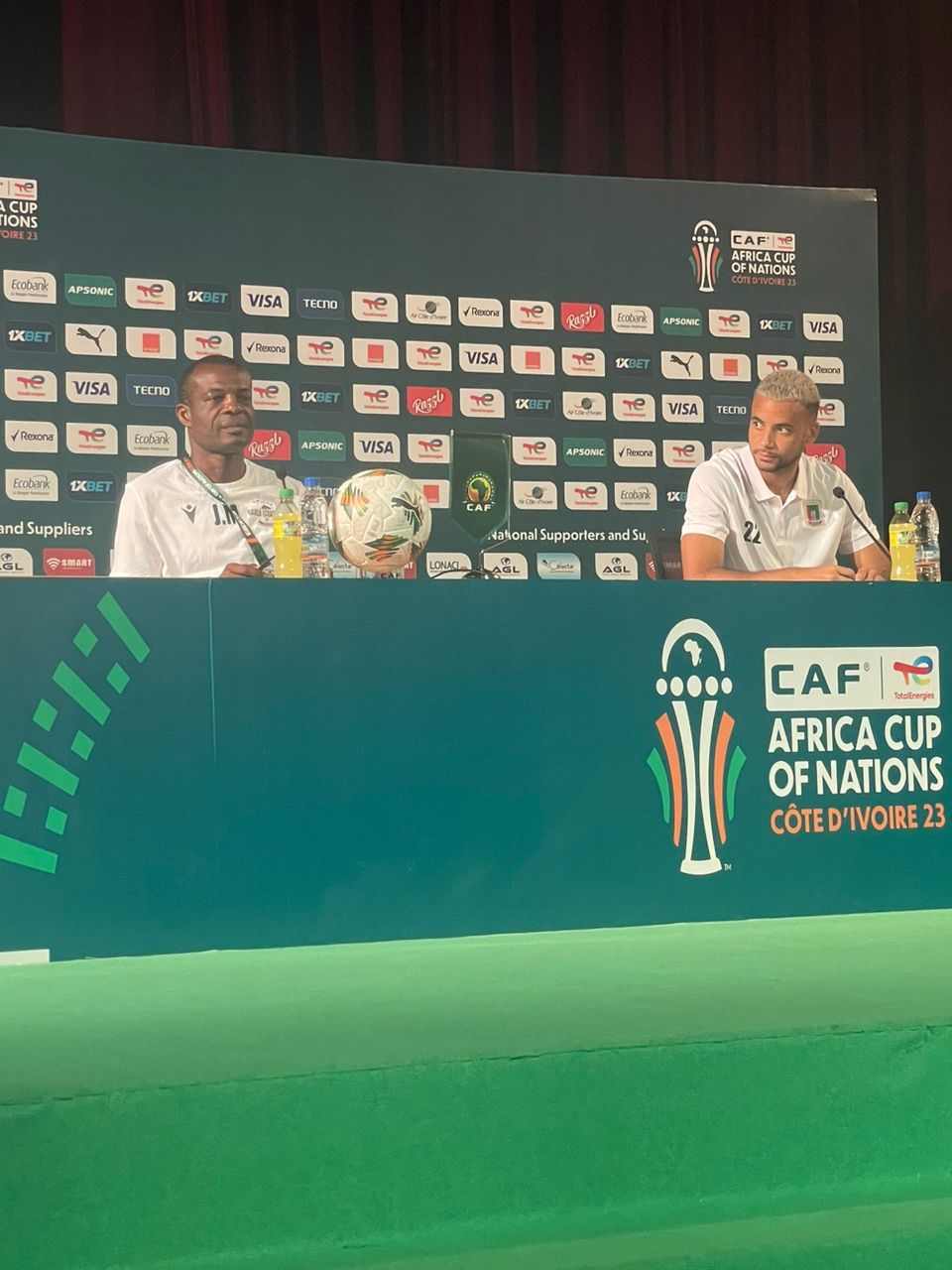 Deux hommes en tenue sportive assis derrière une table lors d’une conférence de presse avec logos d’événement sportif en arrière-plan