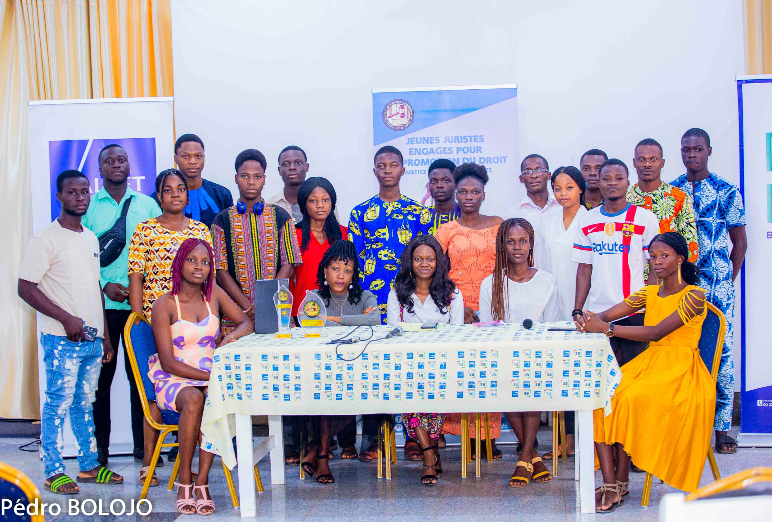 Un groupe de jeunes vêtus de tenues variées posant autour d’une table avec des trophées et des affiches en arrière-plan