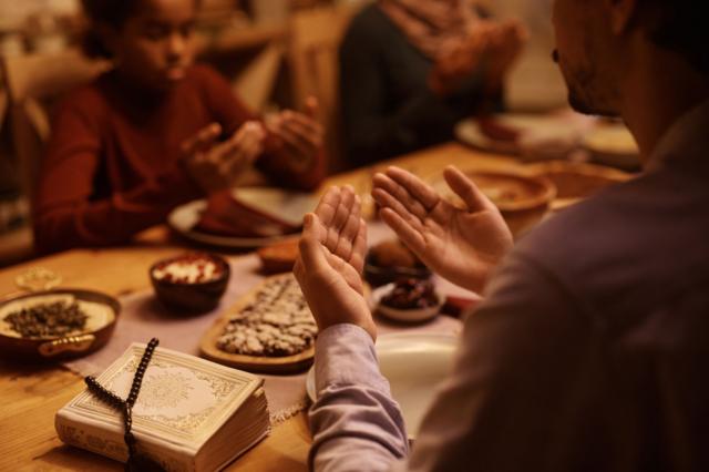 Personnes assises autour d une table en prière pendant un repas avec un livre sacré et un chapelet posés dessus