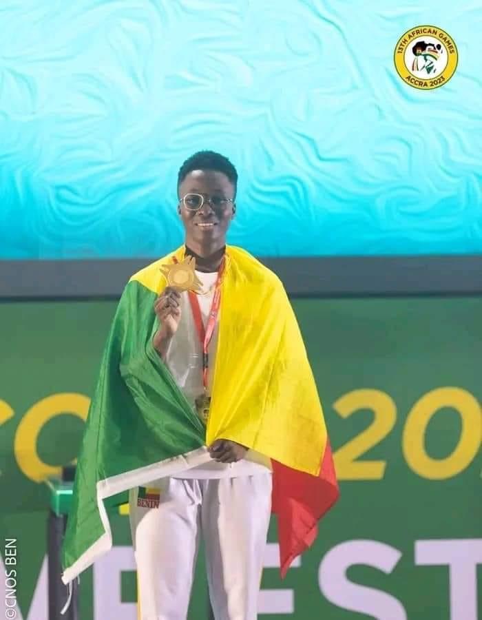 Un sportif souriant drapé dans un drapeau tricolore tenant une médaille d’or avec un décor de jeu en arrière-plan