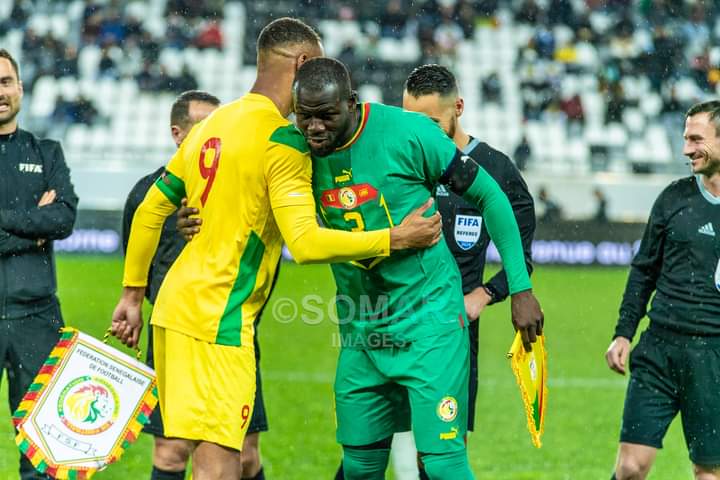 Deux joueurs de football s’embrassent sur le terrain avant le coup d’envoi sous le regard des arbitres et d’autres joueurs