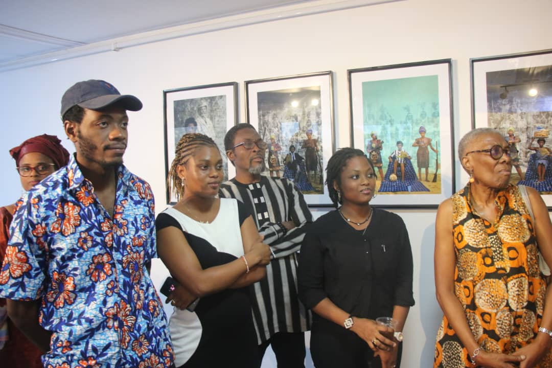 Groupe de sept personnes debout dans une galerie d'art avec plusieurs tableaux encadrés accrochés au mur derrière eux