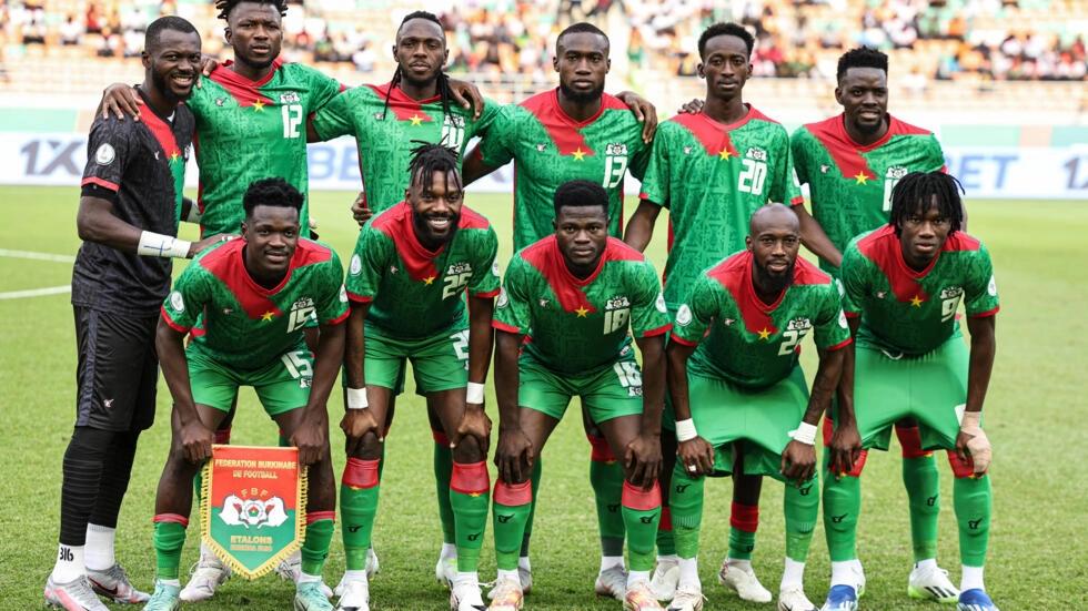 Onze joueurs en maillot vert avec détails rouges posant ensemble sur un terrain de football avant un match