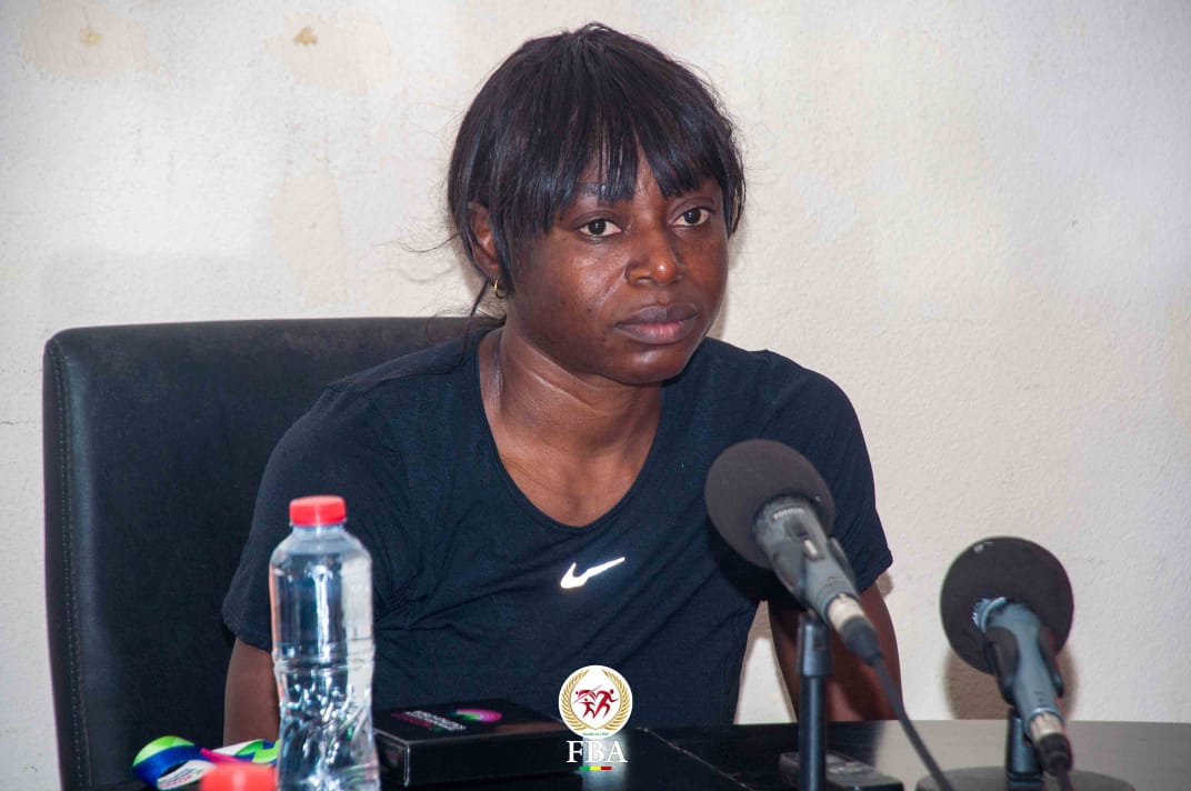 Femme assise devant deux micros et une bouteille d'eau lors d'une conférence dans une pièce claire