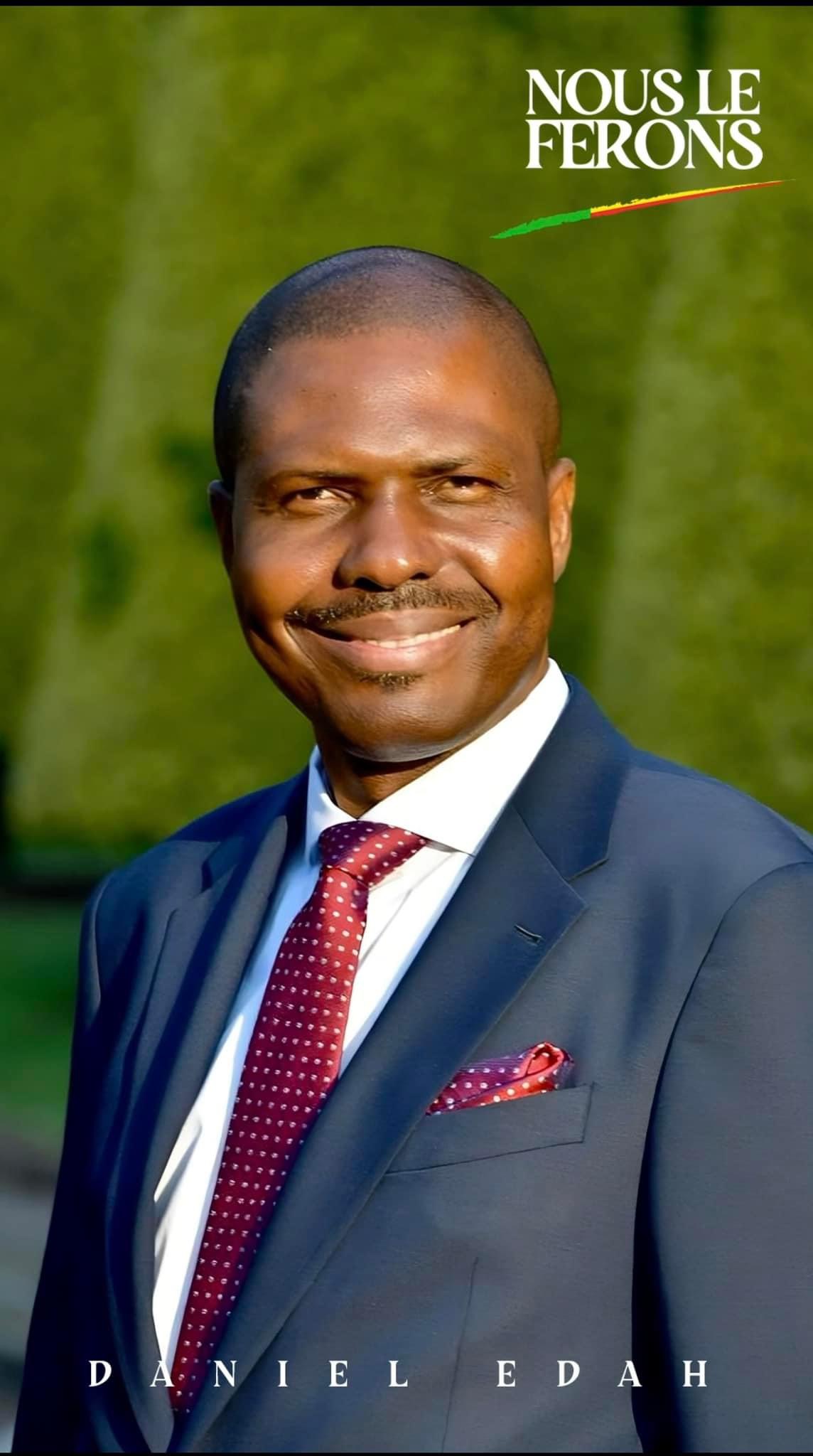 Homme souriant en costume bleu et cravate bordeaux devant un fond flou de verdure avec texte Nous le ferons