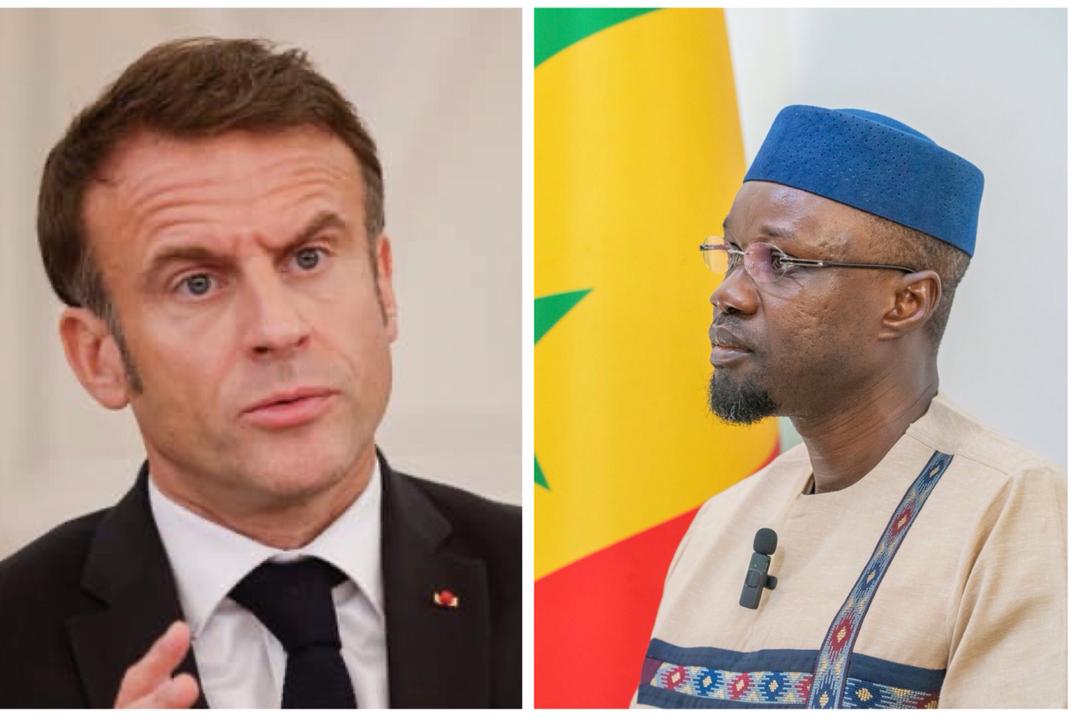 Homme en costume noir parlant et homme en tenue traditionnelle devant un drapeau aux couleurs jaune, vert et rouge