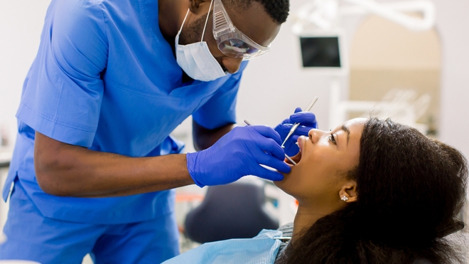 Un professionnel en tenue médicale examine la bouche d'une patiente allongée sur un fauteuil dentaire