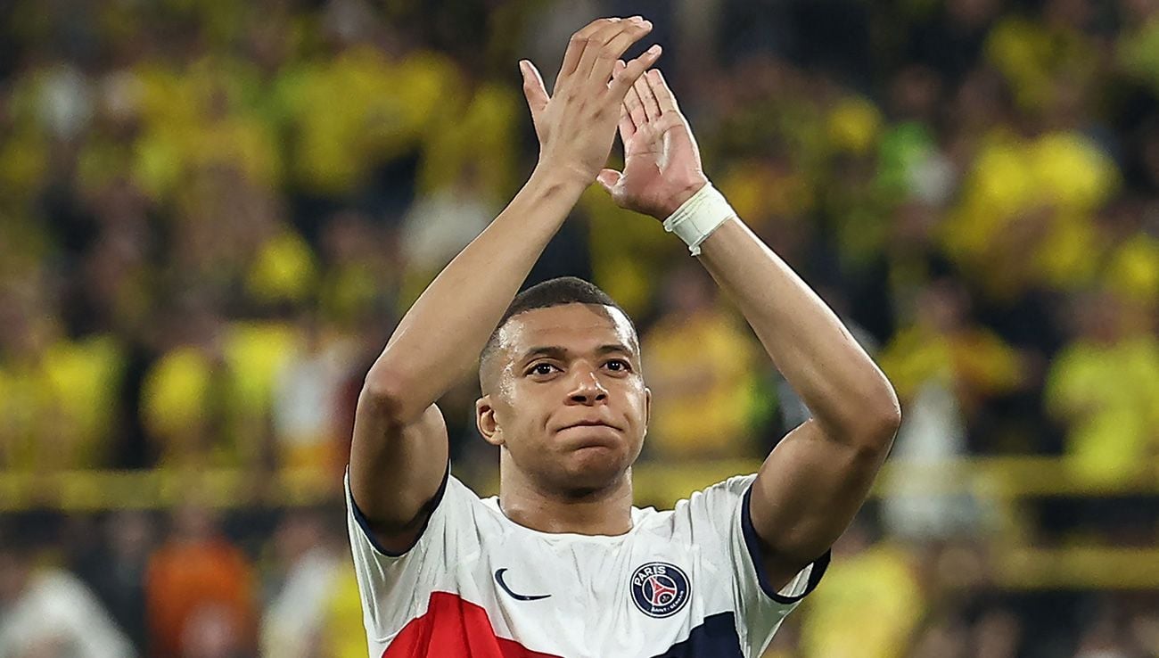 Un joueur de football applaudit avec les mains levées devant un public en tribunes floues dans un stade