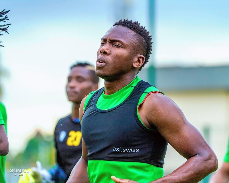 Joueur de football en tenue d'entraînement vert et noir concentré lors d'une séance en extérieur avec d'autres joueurs flous en arrière-plan