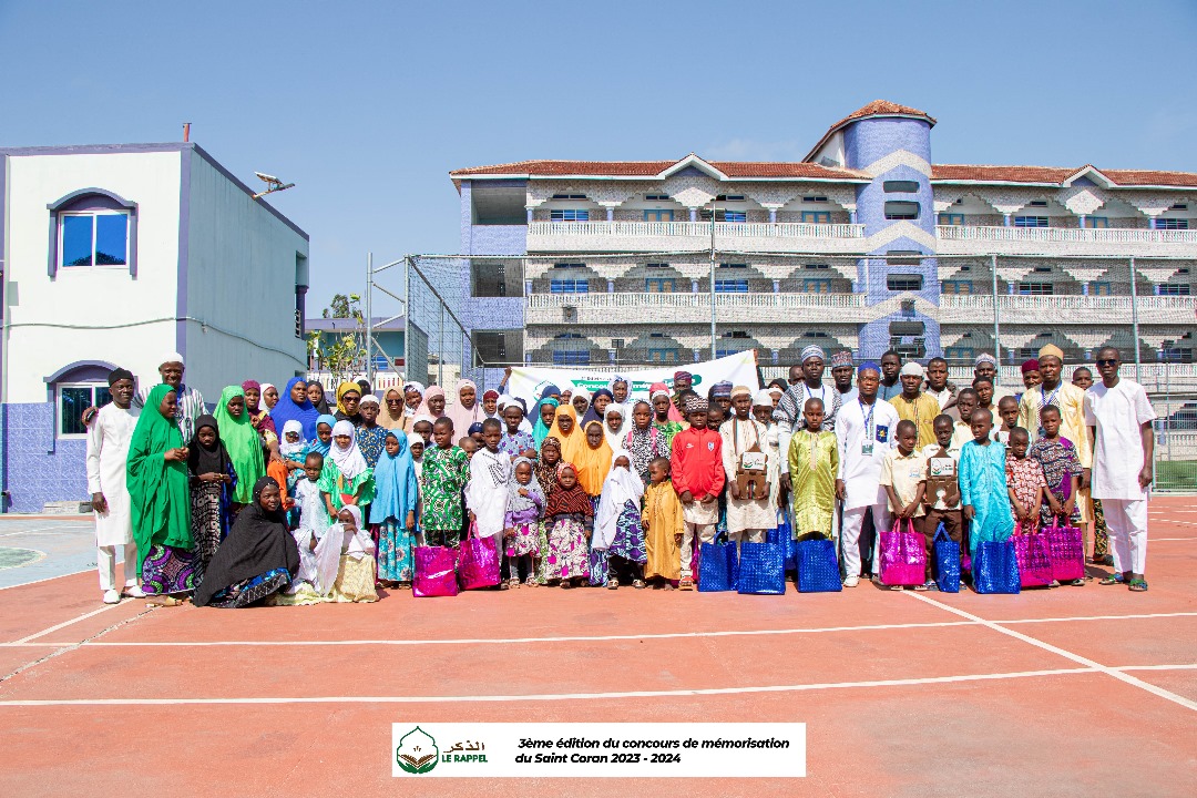 Groupe d’enfants et adultes vêtus de tenues colorées posant devant un bâtiment bleu sous un ciel clair