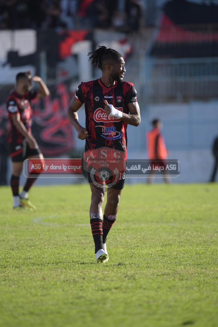 Un joueur de football en tenue rouge et noire court sur le terrain en regardant sur le côté