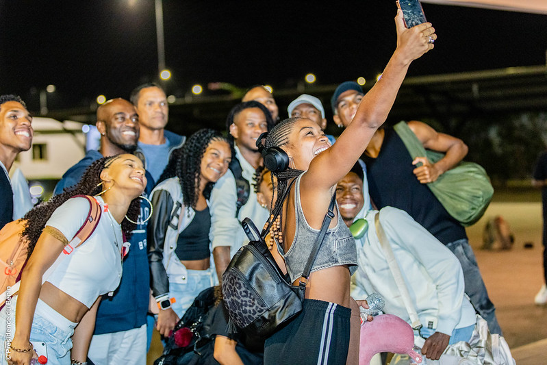 Un groupe de jeunes souriants prennent un selfie la nuit dans un espace extérieur éclairé
