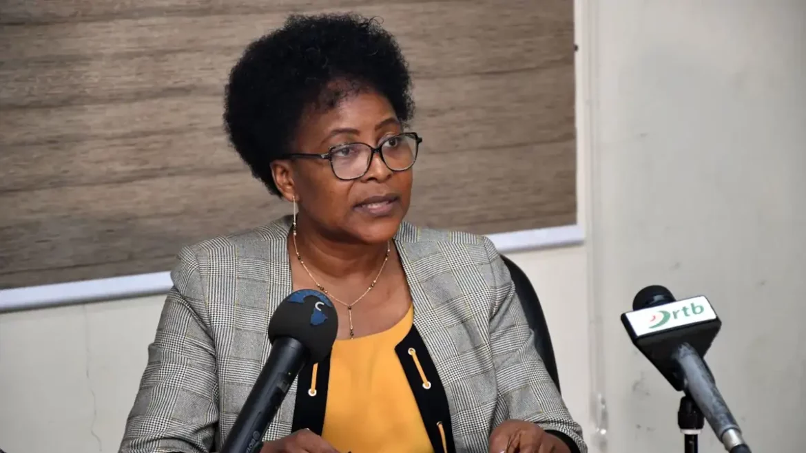 Femme portant des lunettes et un blazer à carreaux parlant devant deux microphones lors d une réunion ou conférence