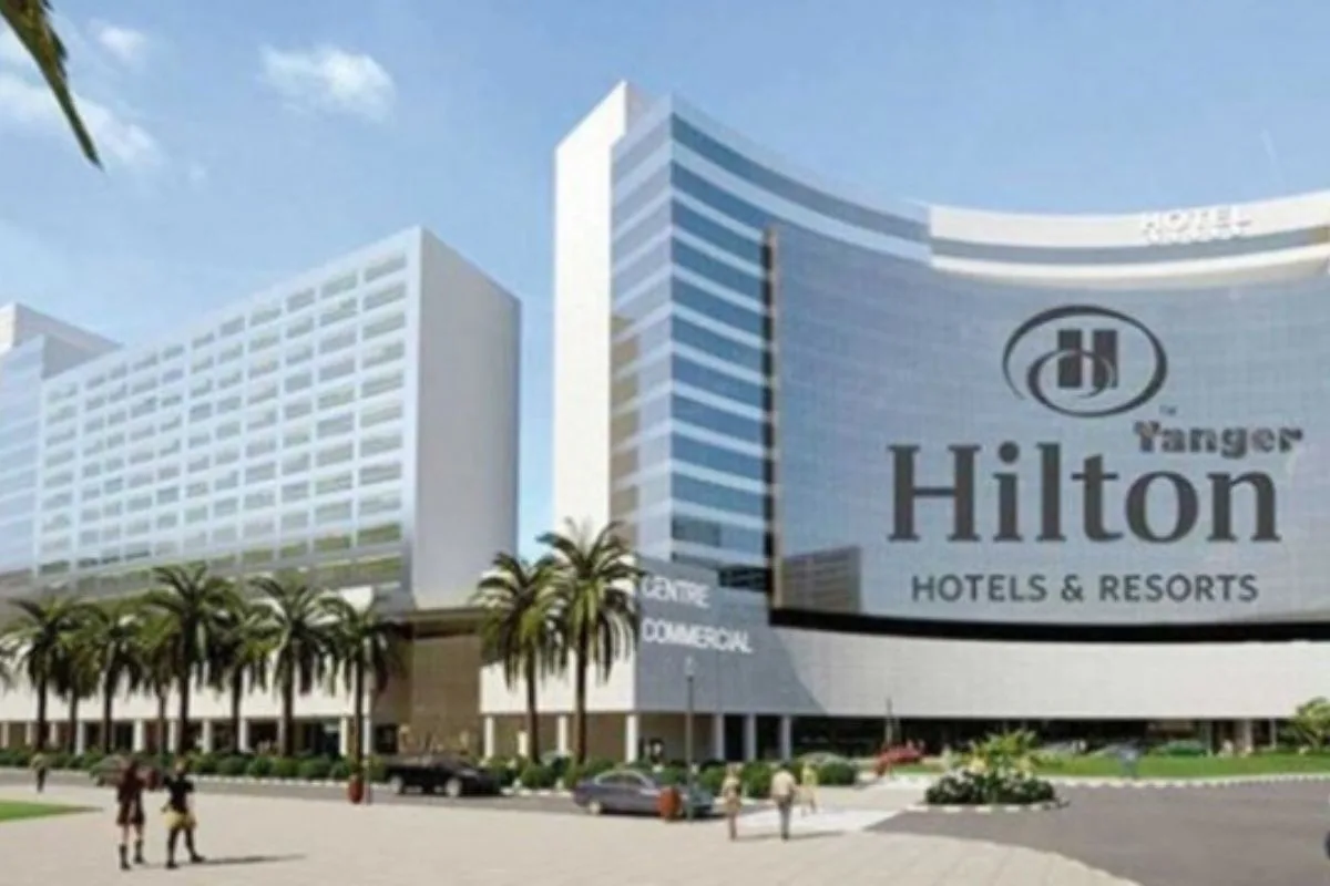 Grands bâtiments modernes avec façades vitrées et palmiers devant un centre commercial affichant logo Hilton Hotels & Resorts