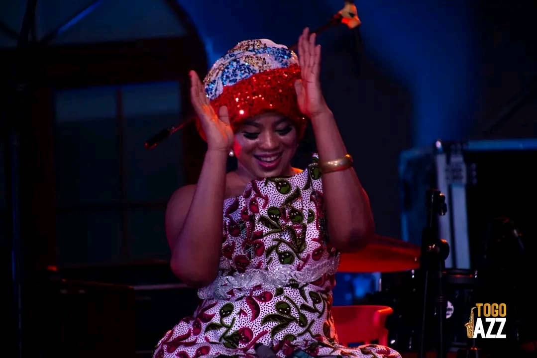 Femme souriante en tenue traditionnelle colorée et coiffe chantant et dansant sur scène éclairée en bleu et rouge