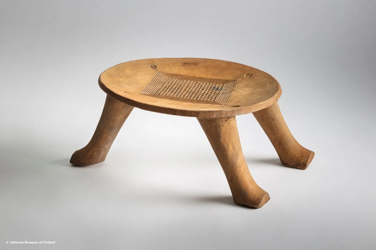 Tabouret en bois clair avec un plateau circulaire orné d'une gravure quadrillée et quatre pieds courbés vers l'extérieur