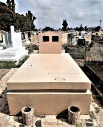 Tombe en pierre claire entourée d'autres sépultures dans un cimetière sous un ciel nuageux