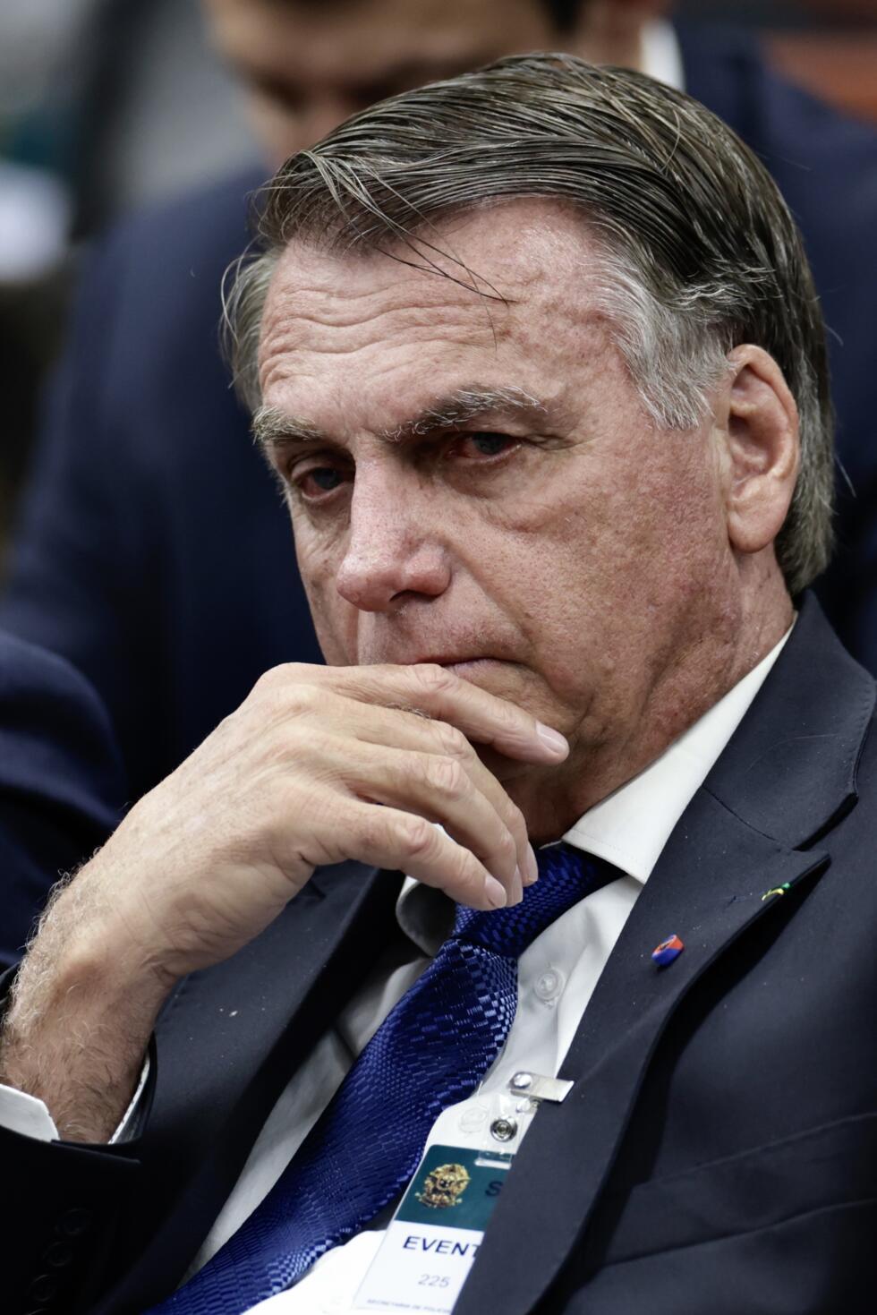 Homme pensif en costume sombre avec une cravate bleue et un badge accroché à sa veste