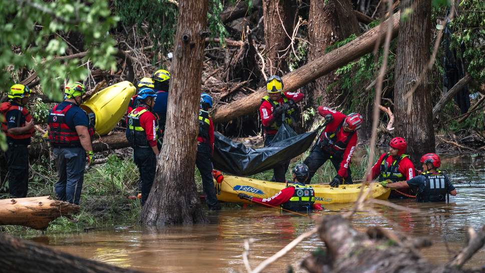 Secouristes en combinaison de sauvetage manœuvrant un kayak près d’arbres tombés dans une zone inondée en forêt