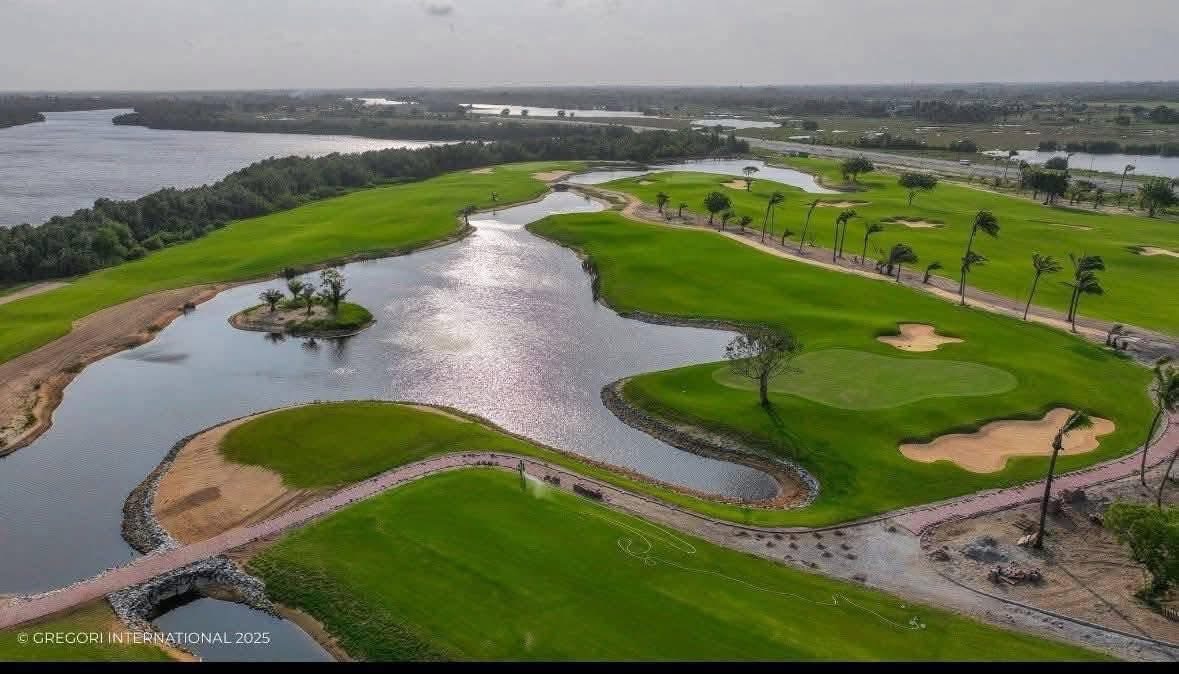 Parcours de golf verdoyant avec étangs et arbres bordant un large cours d'eau sous un ciel nuageux