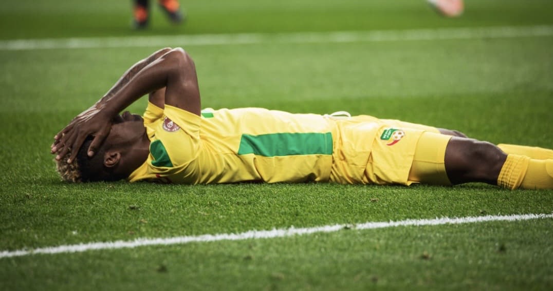 Un joueur de football allongé sur le terrain, les mains sur la tête, semblant déçu ou fatigué