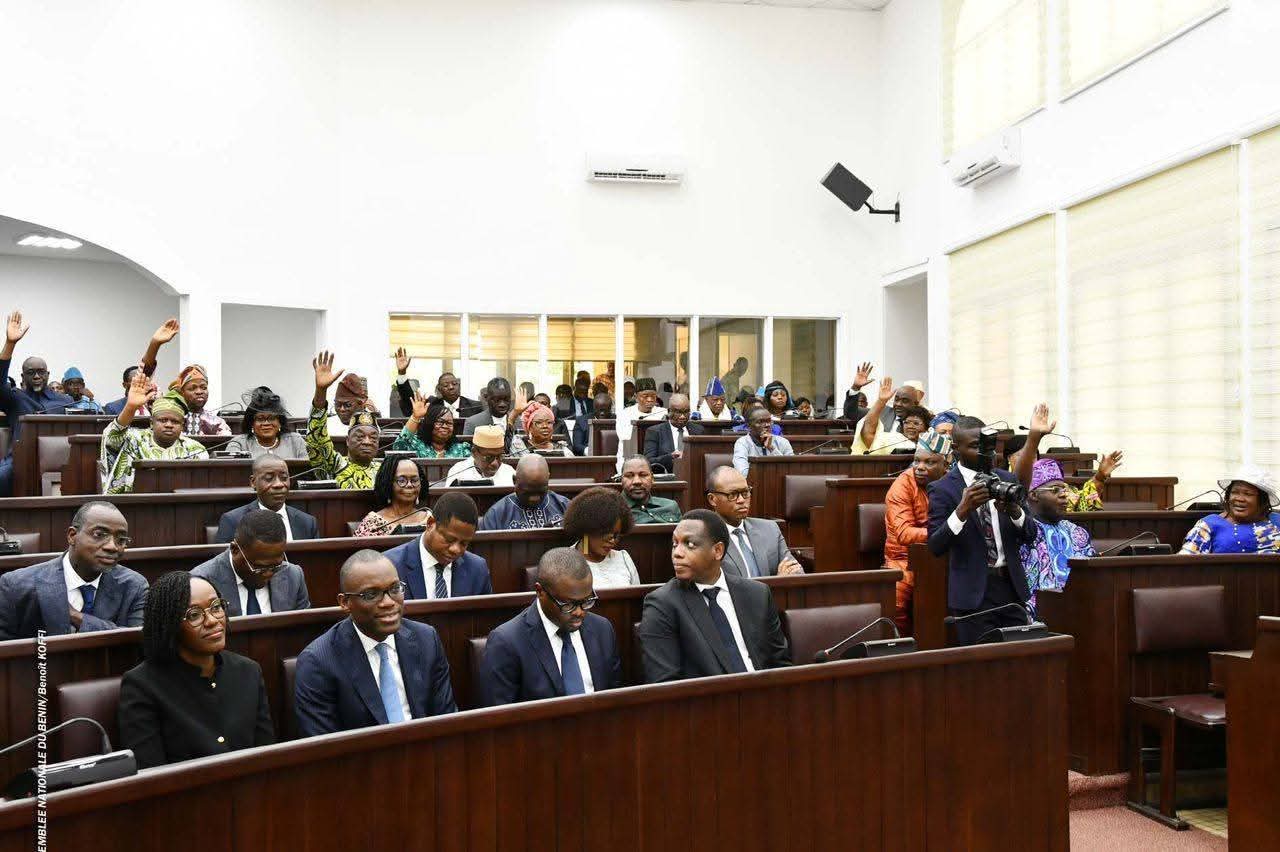 Assemblée réunie en séance avec plusieurs membres levant la main pour voter dans une salle formelle de réunion
