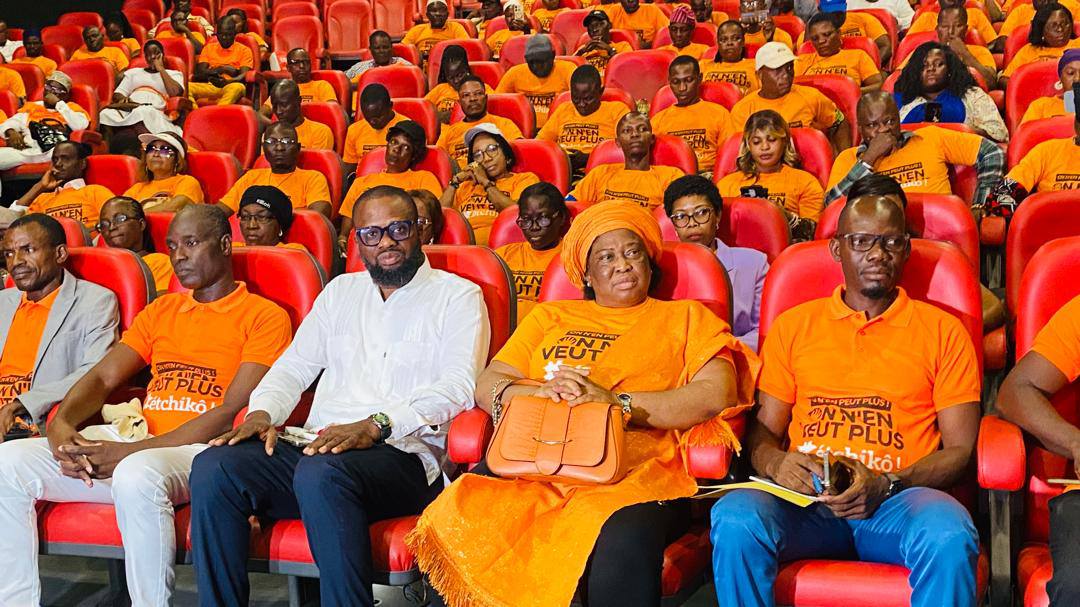 Un groupe de personnes assises dans une salle rouge portant majoritairement des t-shirts orange avec texte imprimé