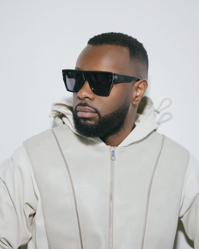 Homme barbu portant un sweat à capuche clair et de grandes lunettes noires regardant sur le côté