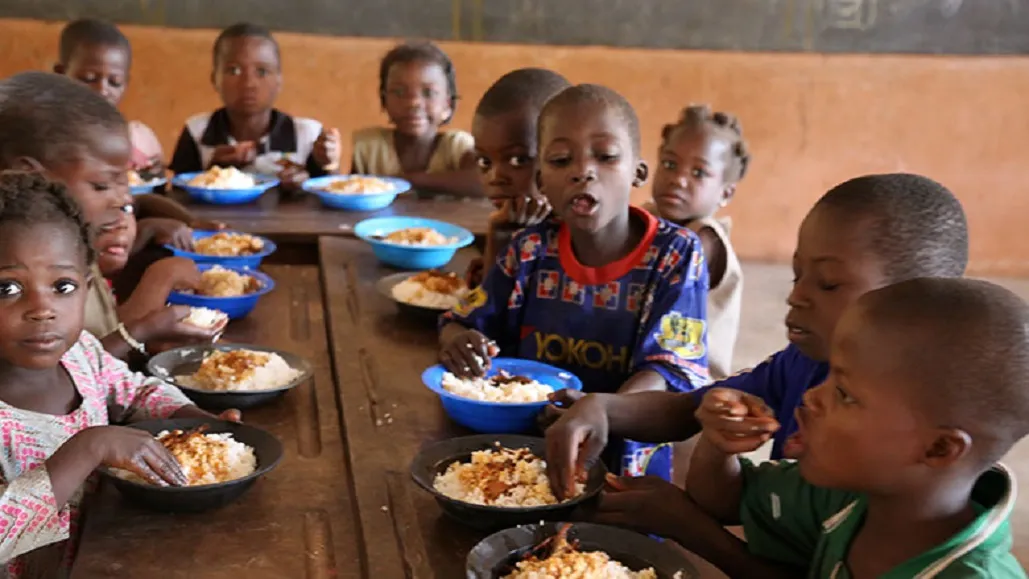 Enfants assis à une table mangeant un repas dans des bols de couleur bleue et noire dans une salle simple