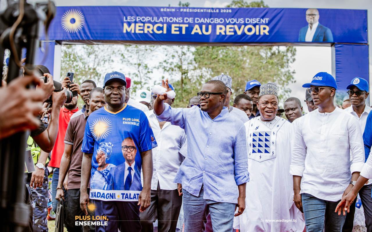Un groupe d'hommes souriant marche sous une banderole de remerciements lors d'un rassemblement politique en extérieur