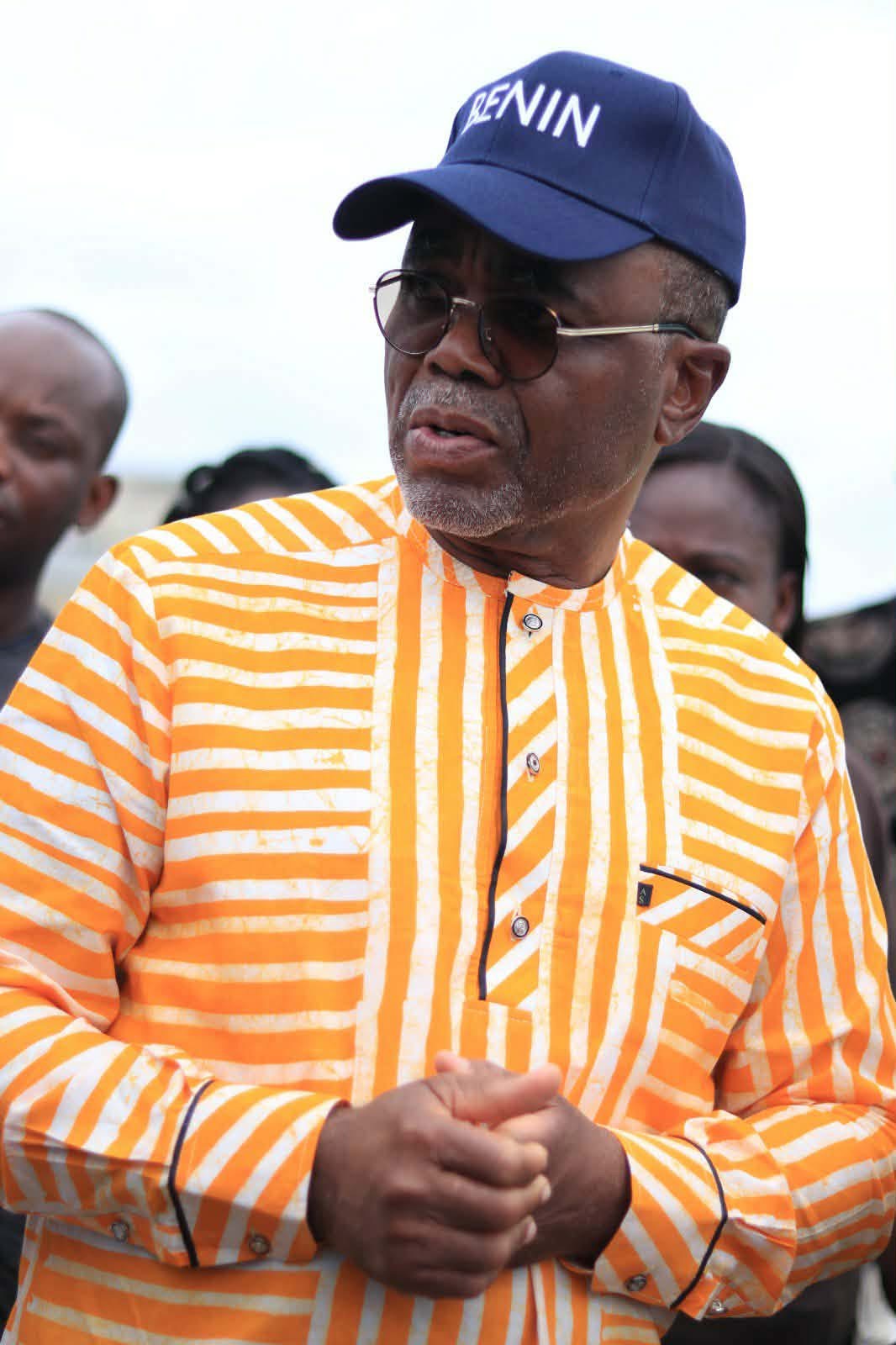 Un homme portant une chemise rayée orange et blanche, une casquette bleue et des lunettes regarde vers la droite avec inquiétude